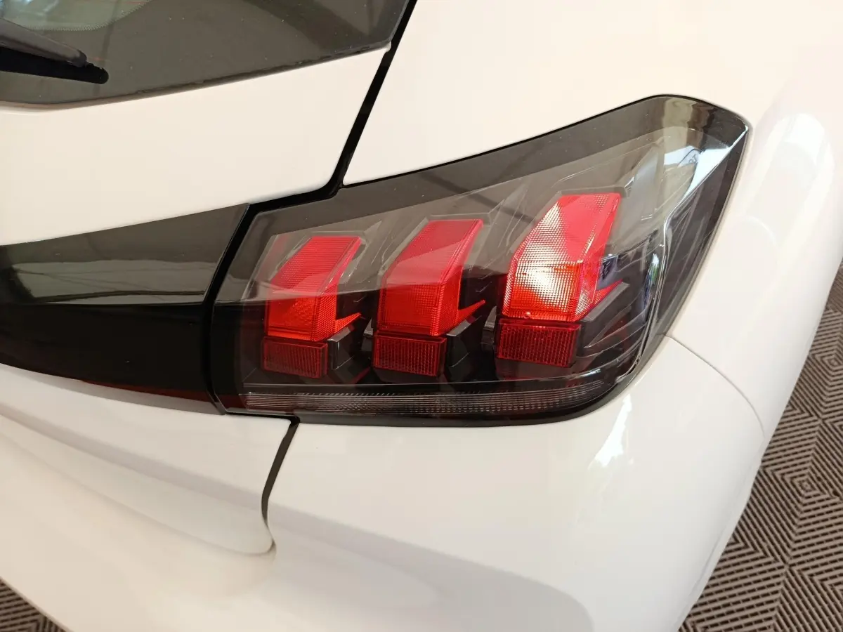Gros plan sur le feu arrière droit rouge et noir d’une Peugeot 208 blanche, version 2023, finition Premium.