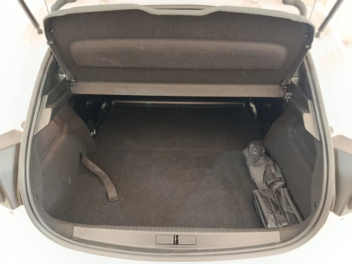 Coffre ouvert vu de dessus d’une Peugeot 208 blanche, montrant un espace de chargement vide avec housse noire sur le côté.