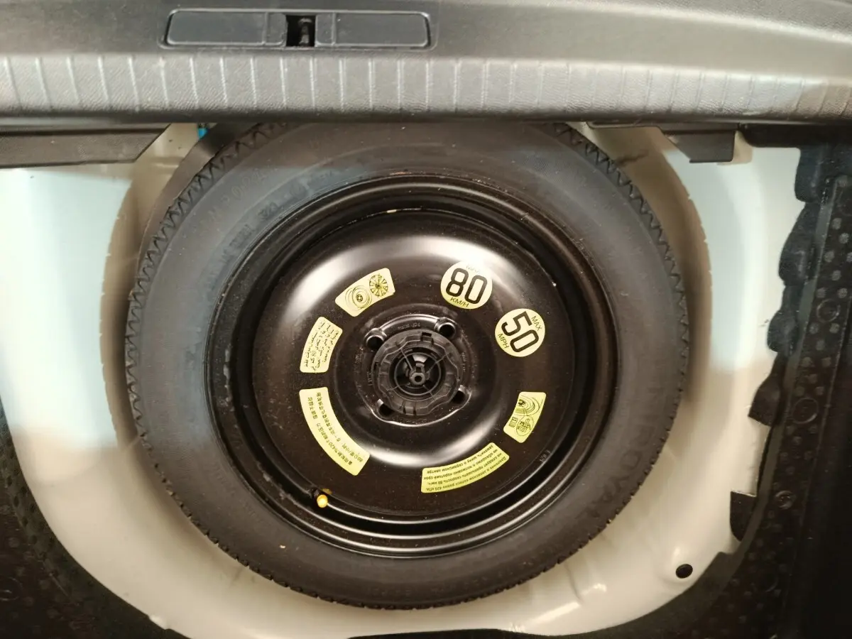 Vue rapprochée de la roue de secours noire dans le coffre blanc d’une Peugeot 208 1.5 BlueHDi 2023.