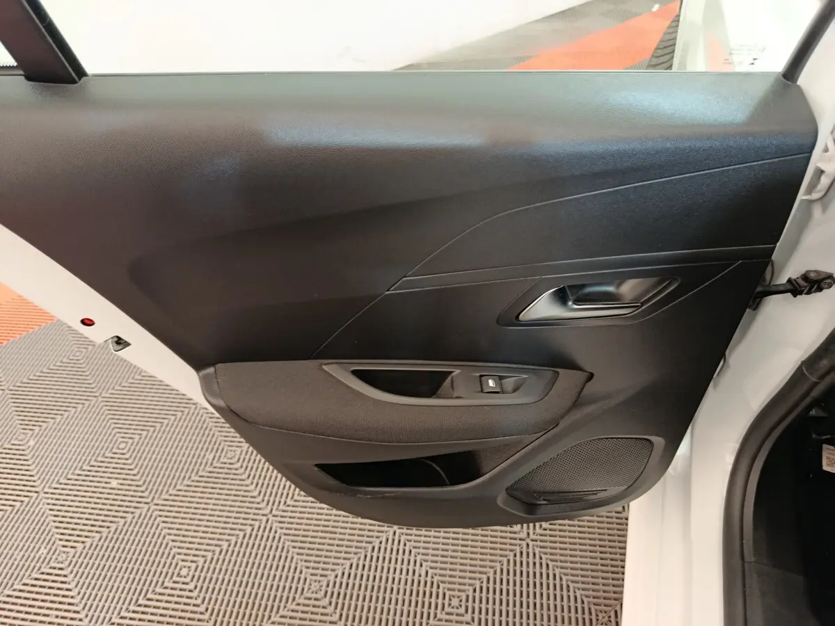Vue intérieure de la porte avant gauche noire du Peugeot 208 blanc, avec poignée et commande de lève-vitre.