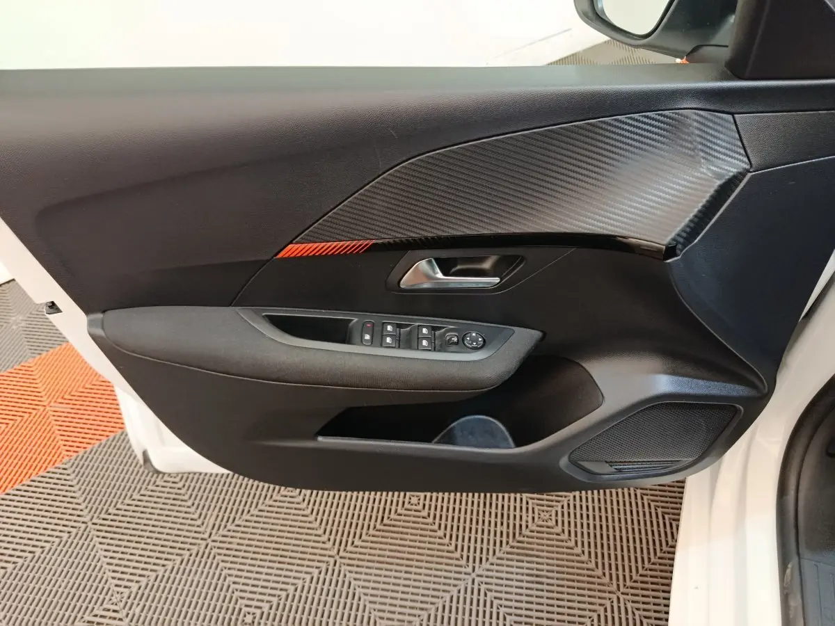 Vue intérieure du panneau de porte avant gauche noir avec insert effet carbone et boutonnerie sur Peugeot 208 blanc 2023.