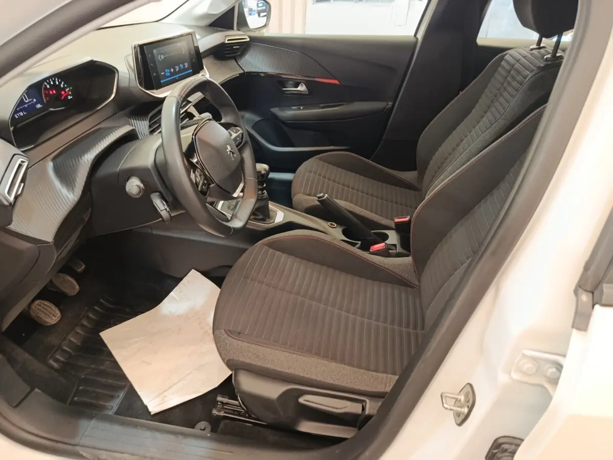 Vue intérieure côté conducteur de la Peugeot 208 blanche 2023, avec volant cuir multifonctions et tableau de bord digital.