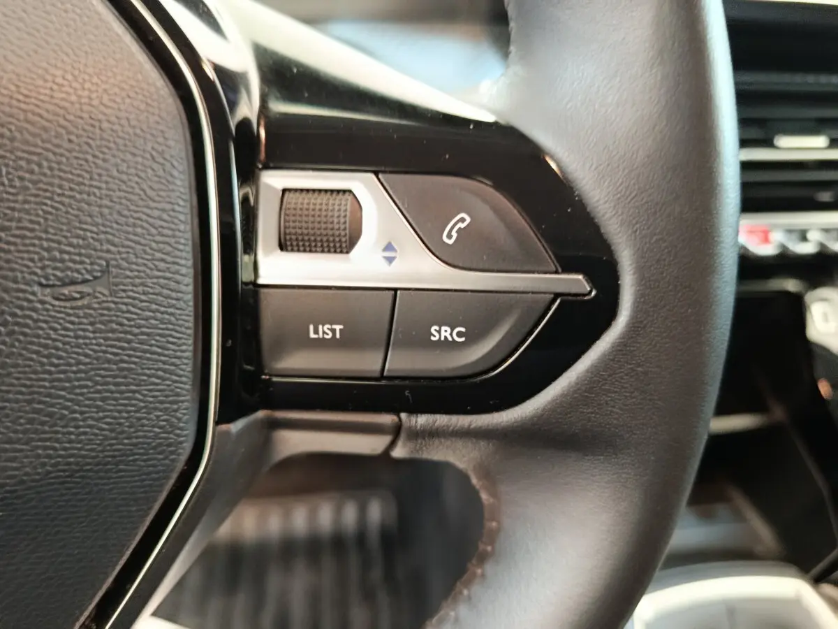 Gros plan sur les commandes gauche du volant cuir noir de la Peugeot 208 1.5 BlueHDi 100 S&S Premium 2023.