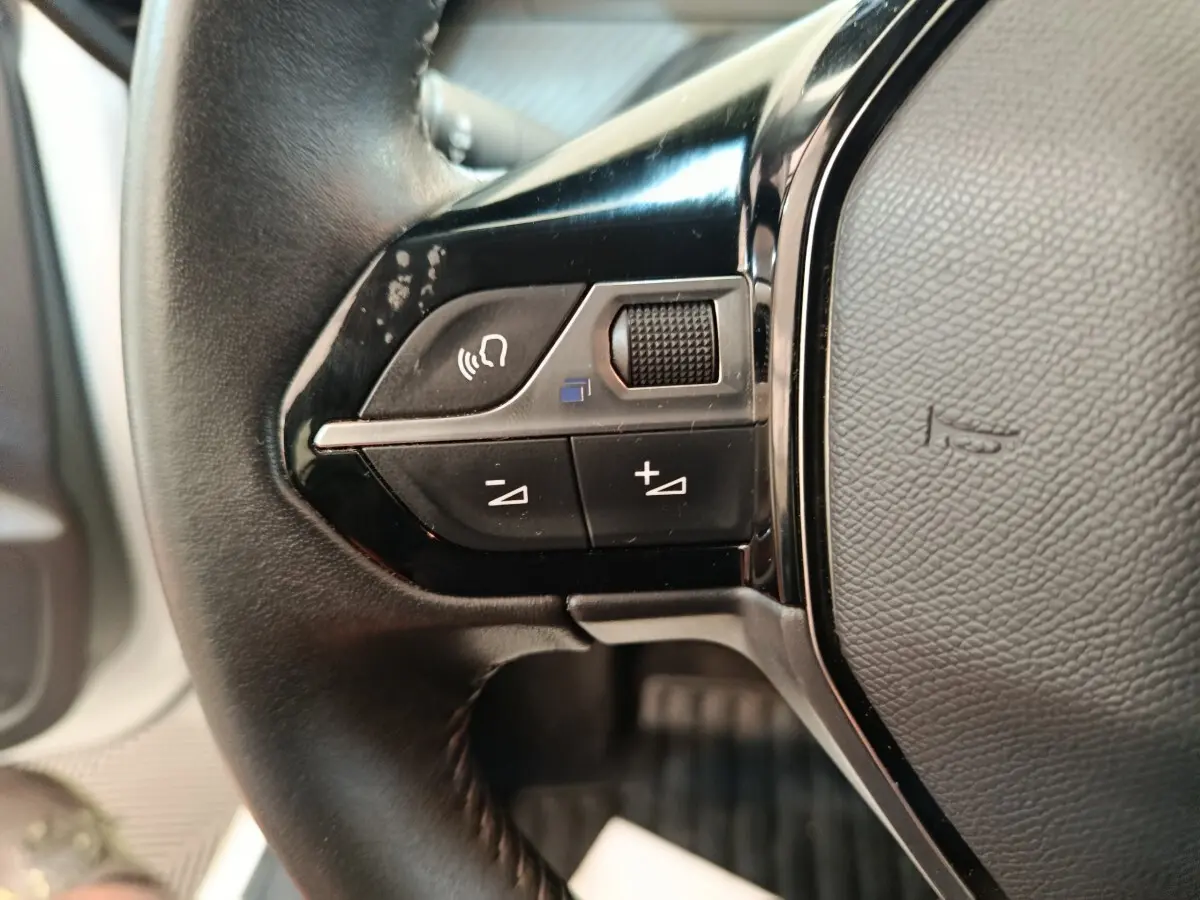 Gros plan sur les commandes gauche du volant cuir noir de la Peugeot 208 1.5 BlueHDi 2023.