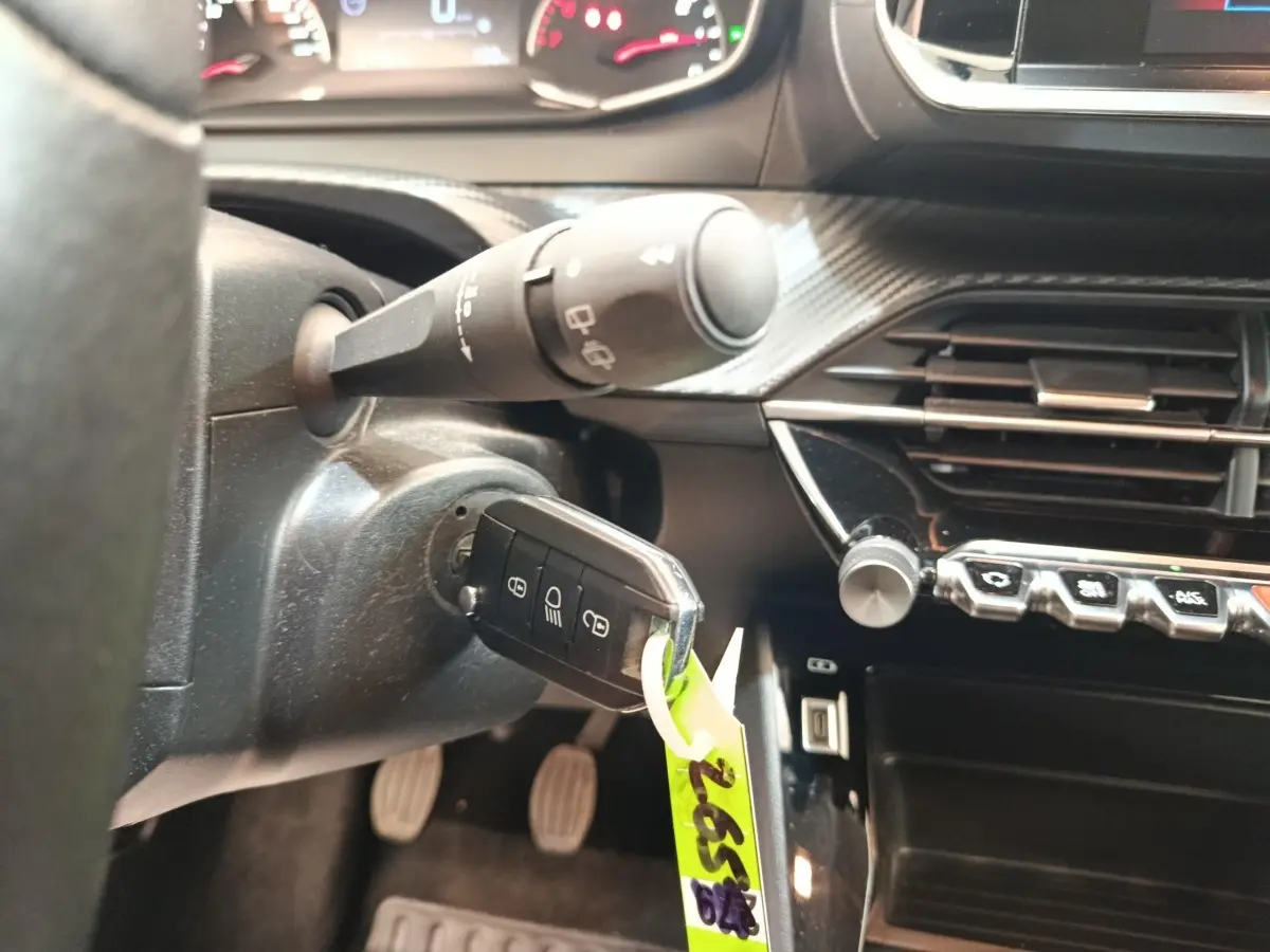 Gros plan intérieur sur le contact et la clé d’une Peugeot 208 blanche, avec tableau de bord et commandes visibles.