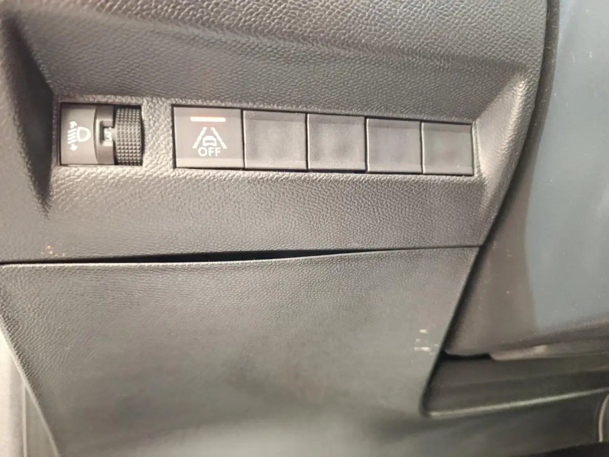 Détail intérieur montrant les commandes de réglage des phares et désactivation de l’assistance au maintien de voie sur Peugeot 208.