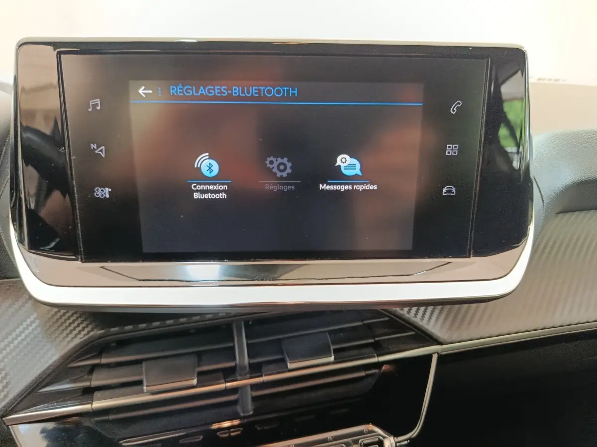 Écran tactile central affichant les réglages Bluetooth dans l’habitacle de la Peugeot 208 blanche, vue de face rapprochée.
