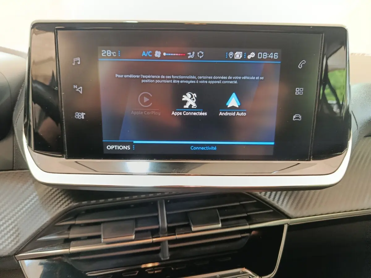 Écran tactile central de la Peugeot 208 2023 affichant Apple CarPlay et Android Auto, avec tableau de bord noir et détails carbone.