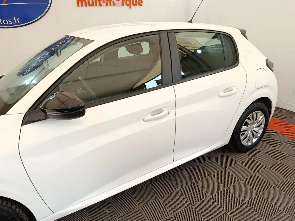 Vue latérale côté gauche d'une Peugeot 208 blanche 2023 avec rétroviseur noir et jantes acier.
