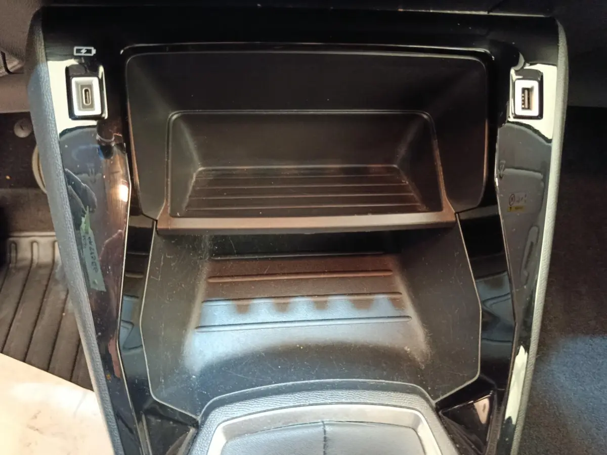 Gros plan sur le rangement central noir brillant de la Peugeot 208 blanc, avec ports USB visibles de chaque côté.