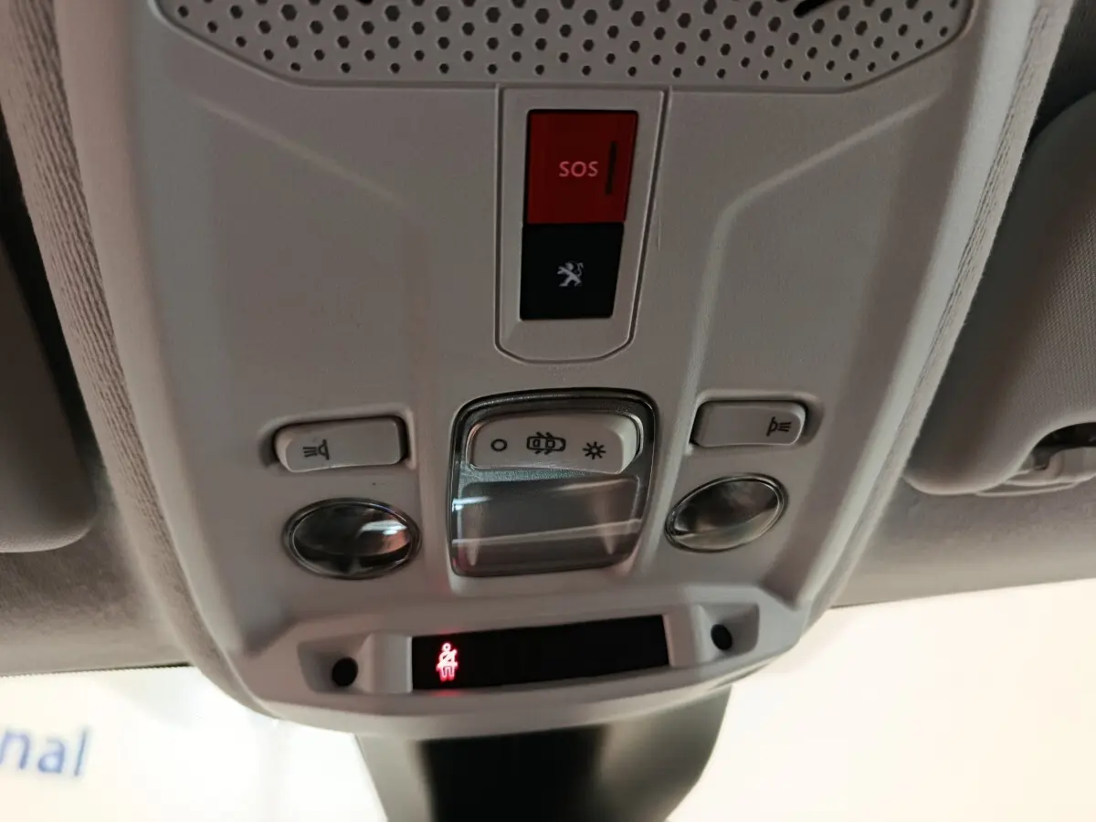 Vue rapprochée du panneau de commandes au plafond intérieur de la Peugeot 208 blanc, avec bouton SOS rouge et éclairage intégré.