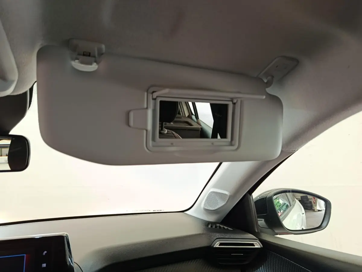 Vue intérieure côté passager du pare-soleil avec miroir ouvert sur Peugeot 208 blanc 2023, tableau de bord et rétroviseur visibles.