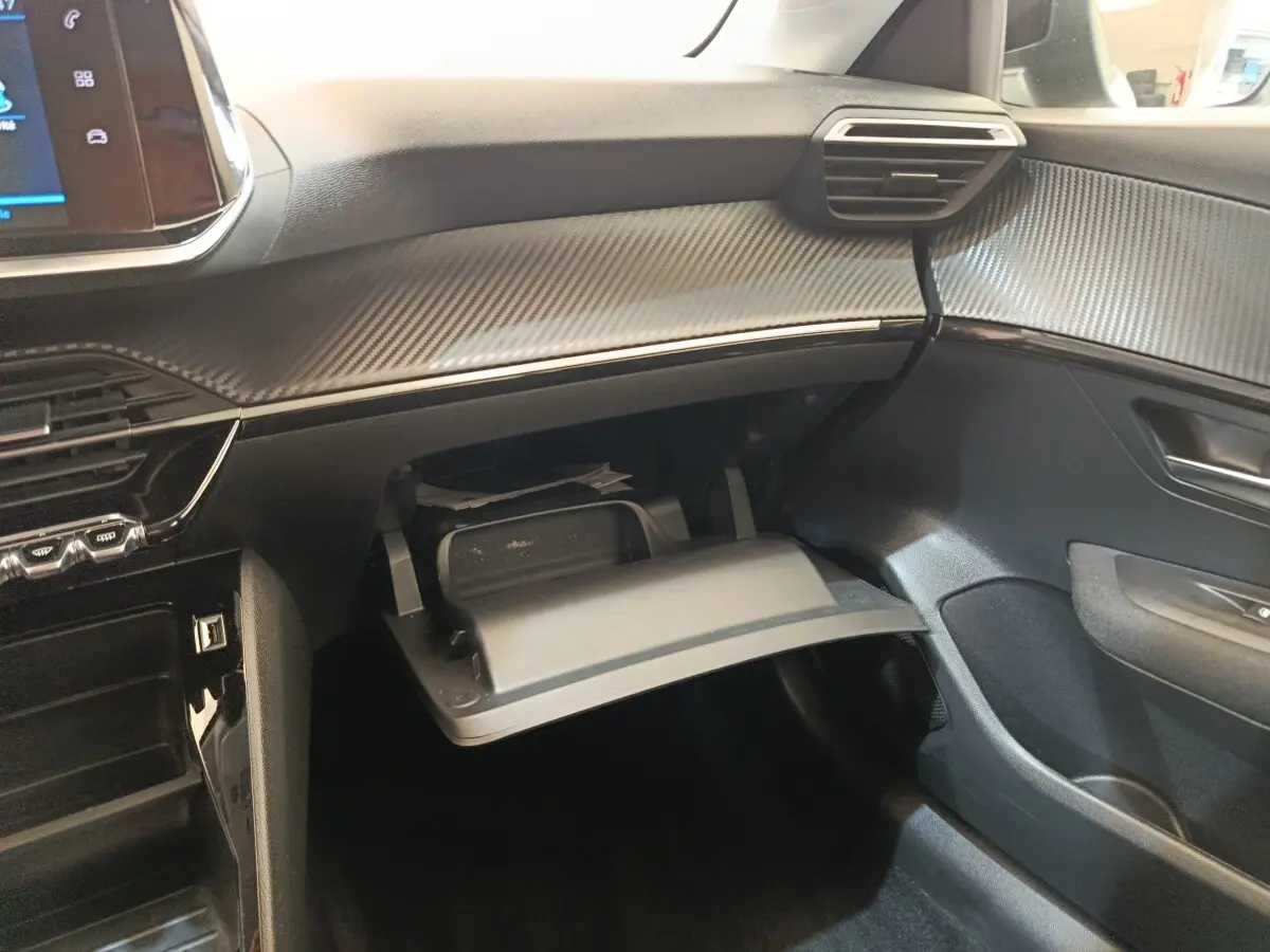 Intérieur de la Peugeot 208 1.5 BlueHDi 2023, vue côté passager sur boîte à gants ouverte et tableau de bord noir texturé.