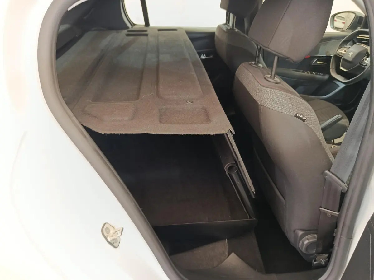 Vue intérieure arrière droite d’une Peugeot 208 blanche 2023, montrant la banquette rabattue et le siège avant en tissu gris.