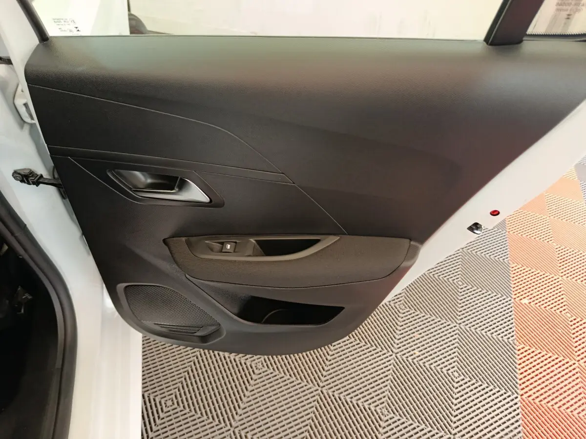 Vue rapprochée de la porte arrière gauche blanche de la Peugeot 208 2023 avec panneau intérieur noir et commande de vitre.
