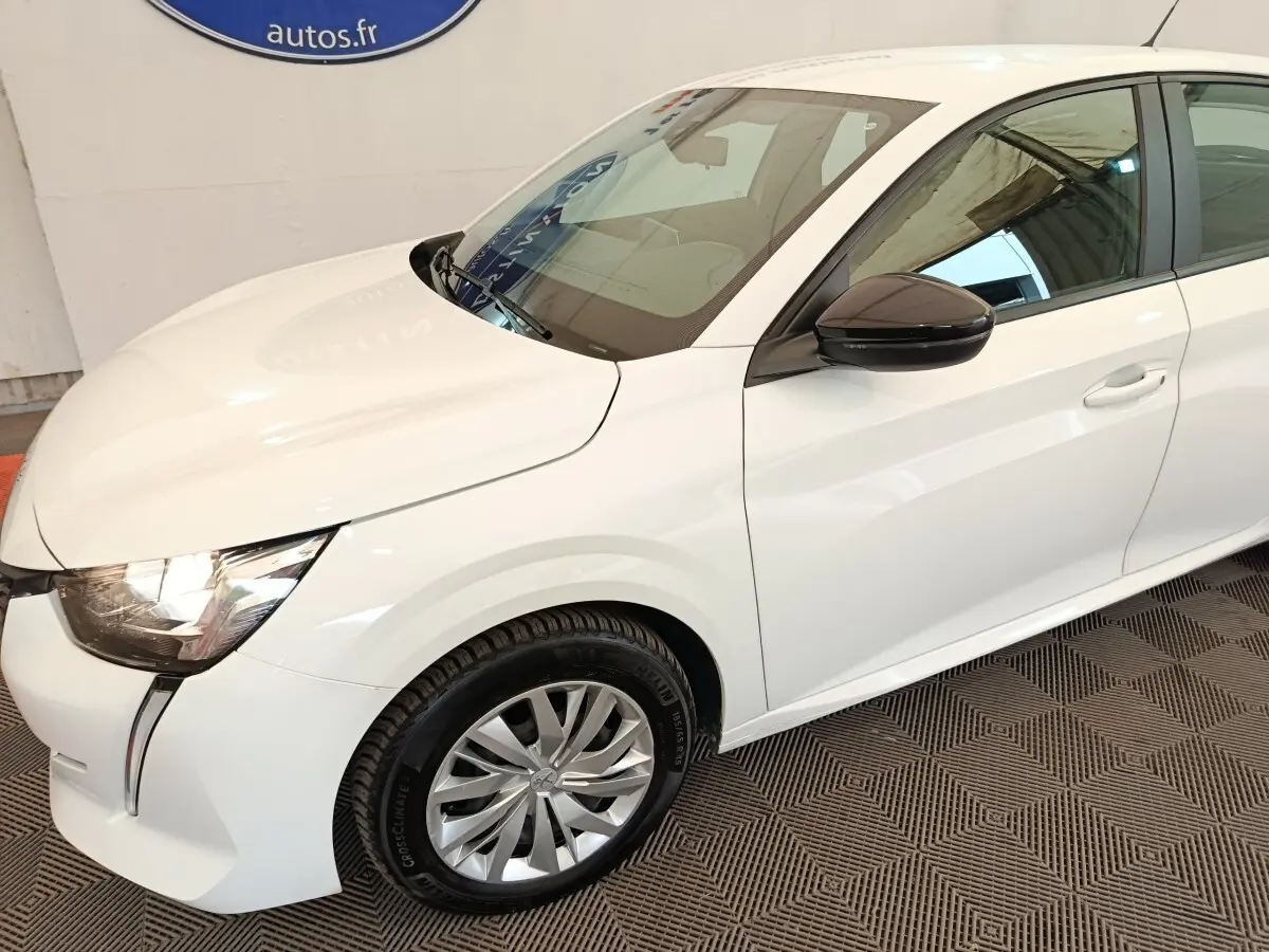 Peugeot 208 blanche vue 3/4 avant droit, avec rétroviseur noir et jantes alliage distinctives.