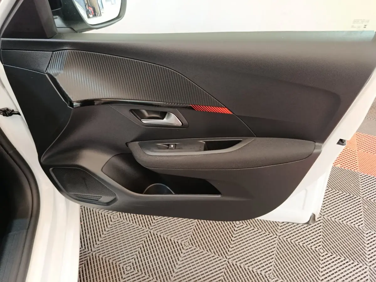 Vue intérieure de la porte avant gauche noire avec insert décoratif rouge de la Peugeot 208 blanche 2023.