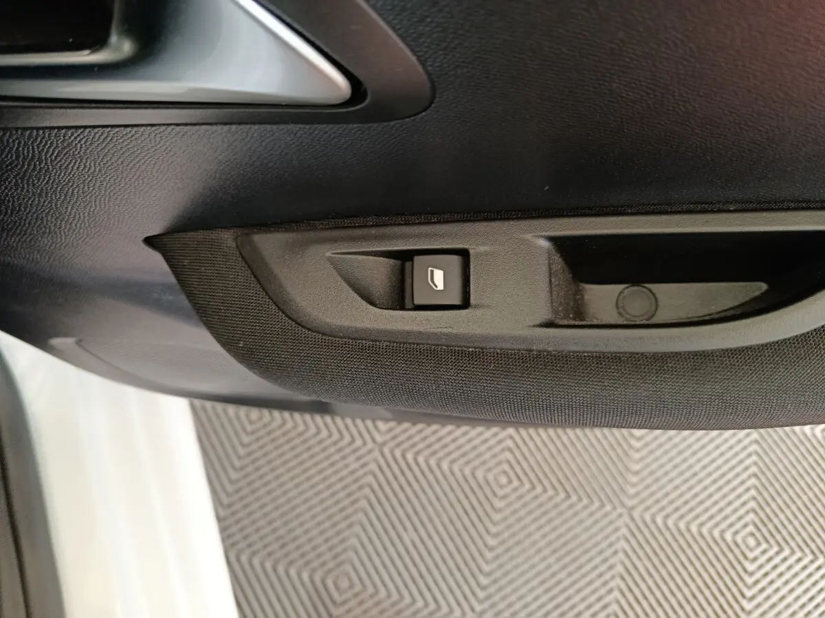 Détail du bouton de commande de lève-vitre sur la porte côté gauche d'une Peugeot 208 blanche 2023.