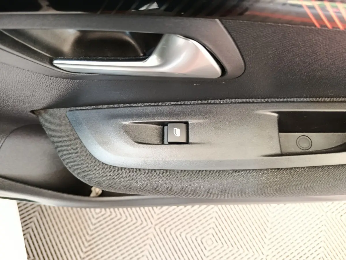 Gros plan sur la poignée intérieure et le bouton de lève-vitre côté gauche de la porte d’une Peugeot 208 blanche.