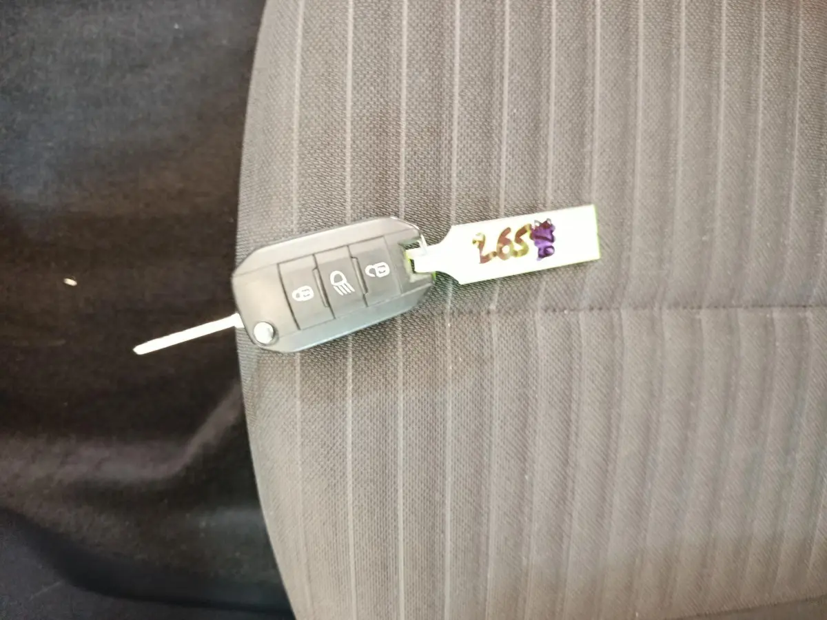 Clé de voiture Peugeot 208 posée sur un siège tissu gris foncé à rayures verticales.