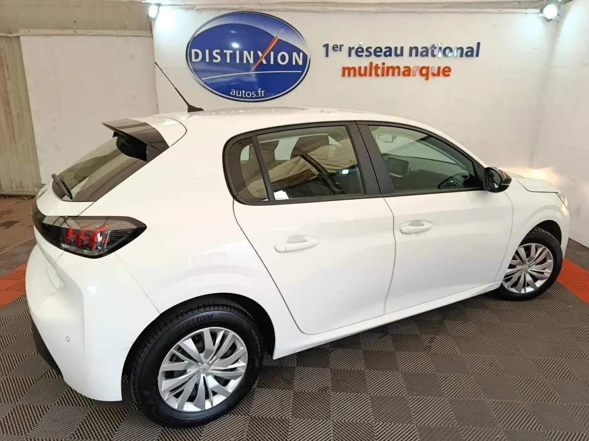 Vue 3/4 arrière droite d'une Peugeot 208 blanche 2023 dans un showroom avec jantes alliage et feux arrière LED.