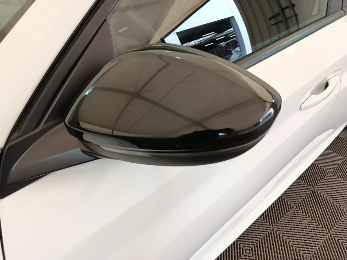 Rétroviseur noir côté gauche en gros plan sur Peugeot 208 blanche vue partielle de la porte avant.