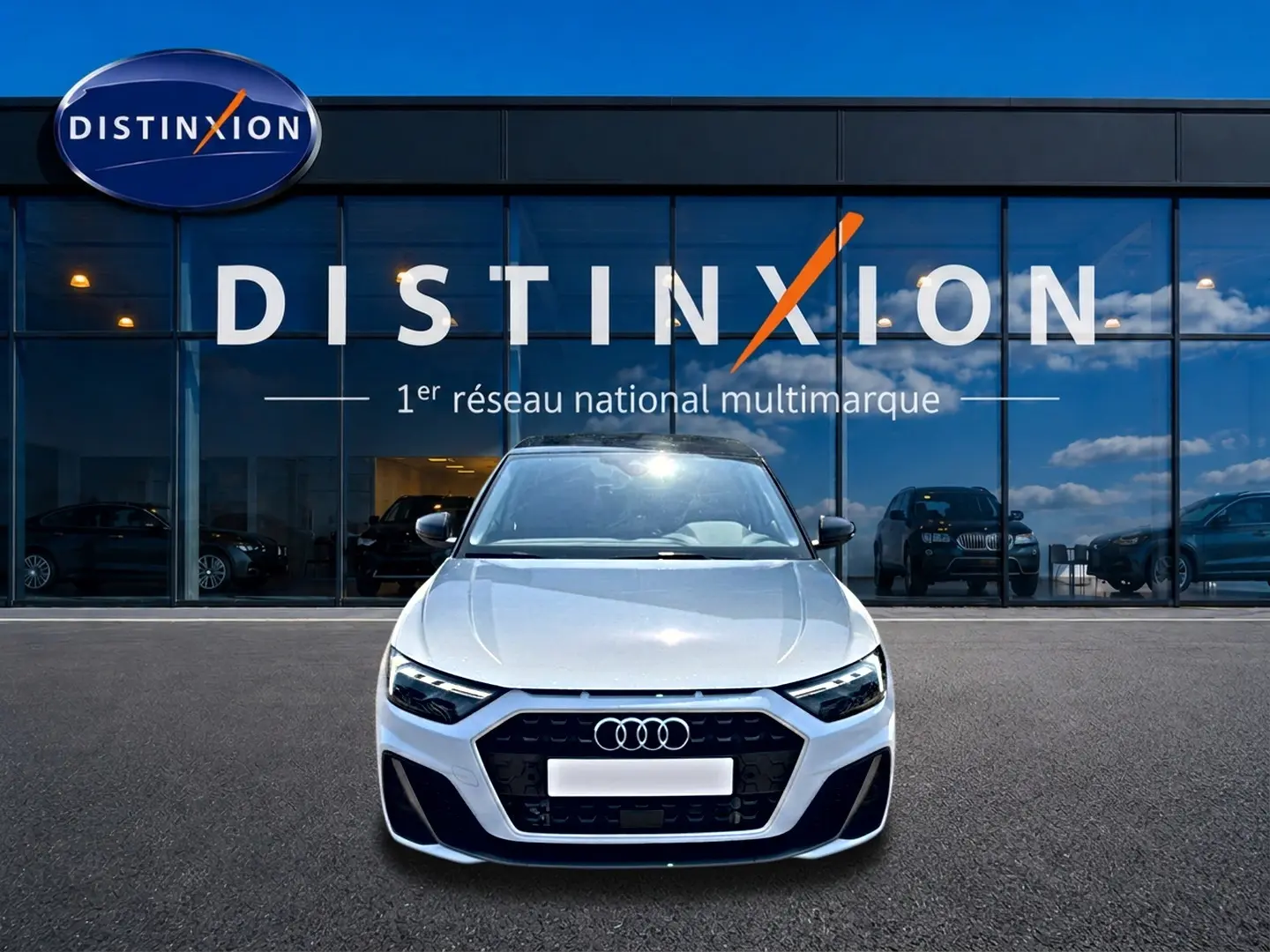 Vue avant d'une Audi A1 Sportback 30 TFSI blanche avec calandre noire et logo Audi, devant une vitrine Distinxion.