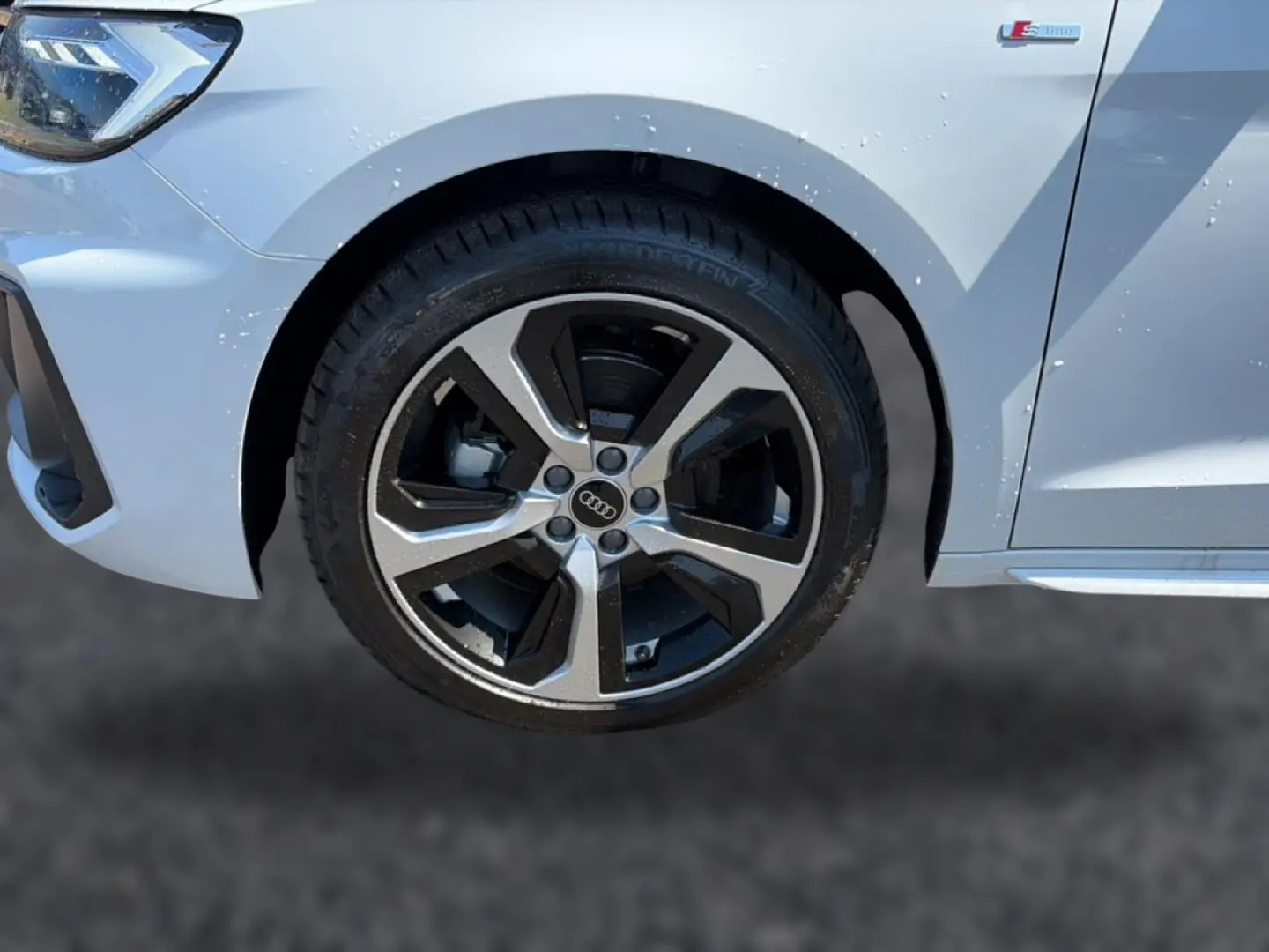 Gros plan sur la roue avant gauche et l’aile blanche d’une Audi A1 Sportback 30 TFSI S line 2026 avec jante alu bicolore.