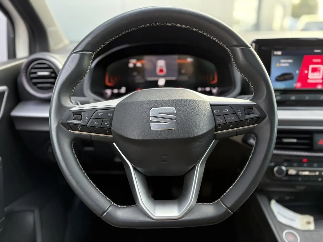 Gros plan sur le volant cuir multifonction à méplat de la SEAT IBIZA TSI 115 Xcellence, tableau de bord numérique visible.