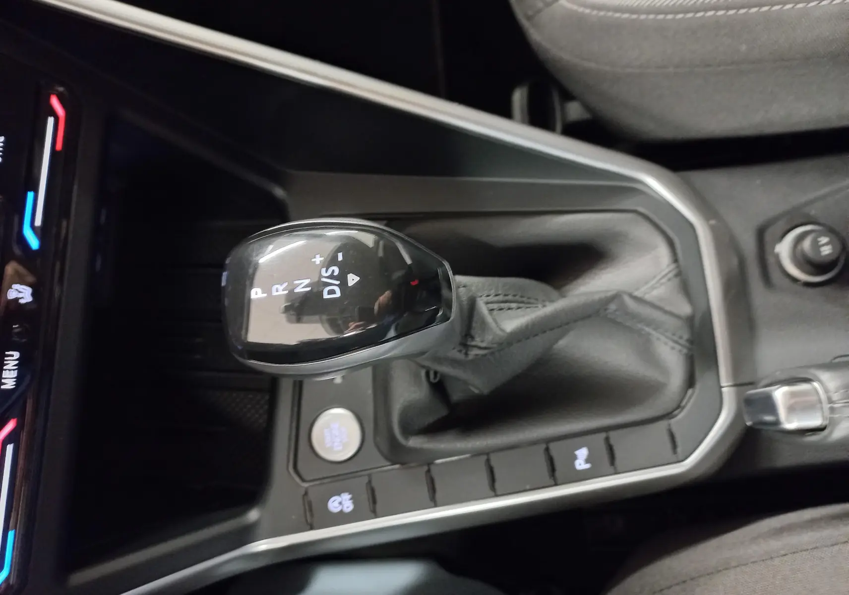 Le levier de vitesse automatique noir du Volkswagen Taigo 1.0 TSI 116 DSG7 VW Edition vu de dessus, entouré de commandes.