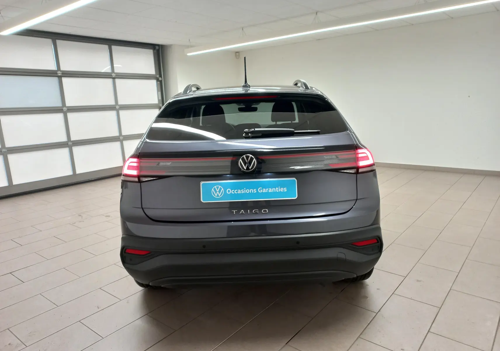 Vue arrière d'un Volkswagen Taigo gris cendré 2025 avec feux LED allumés dans un garage lumineux.