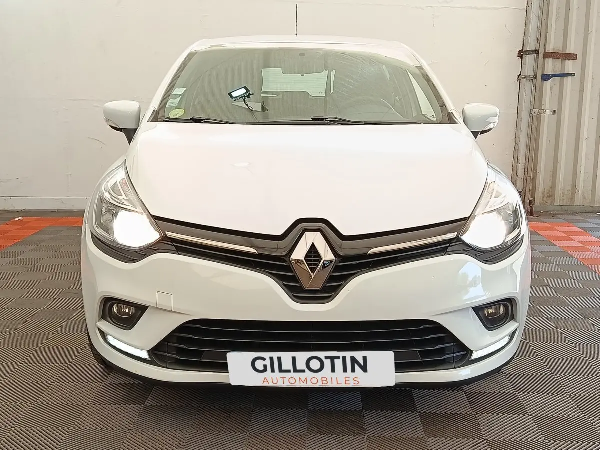 Vue frontale d'une Renault Clio Business dCi 75 blanche avec phares allumés et calandre noire brillante.