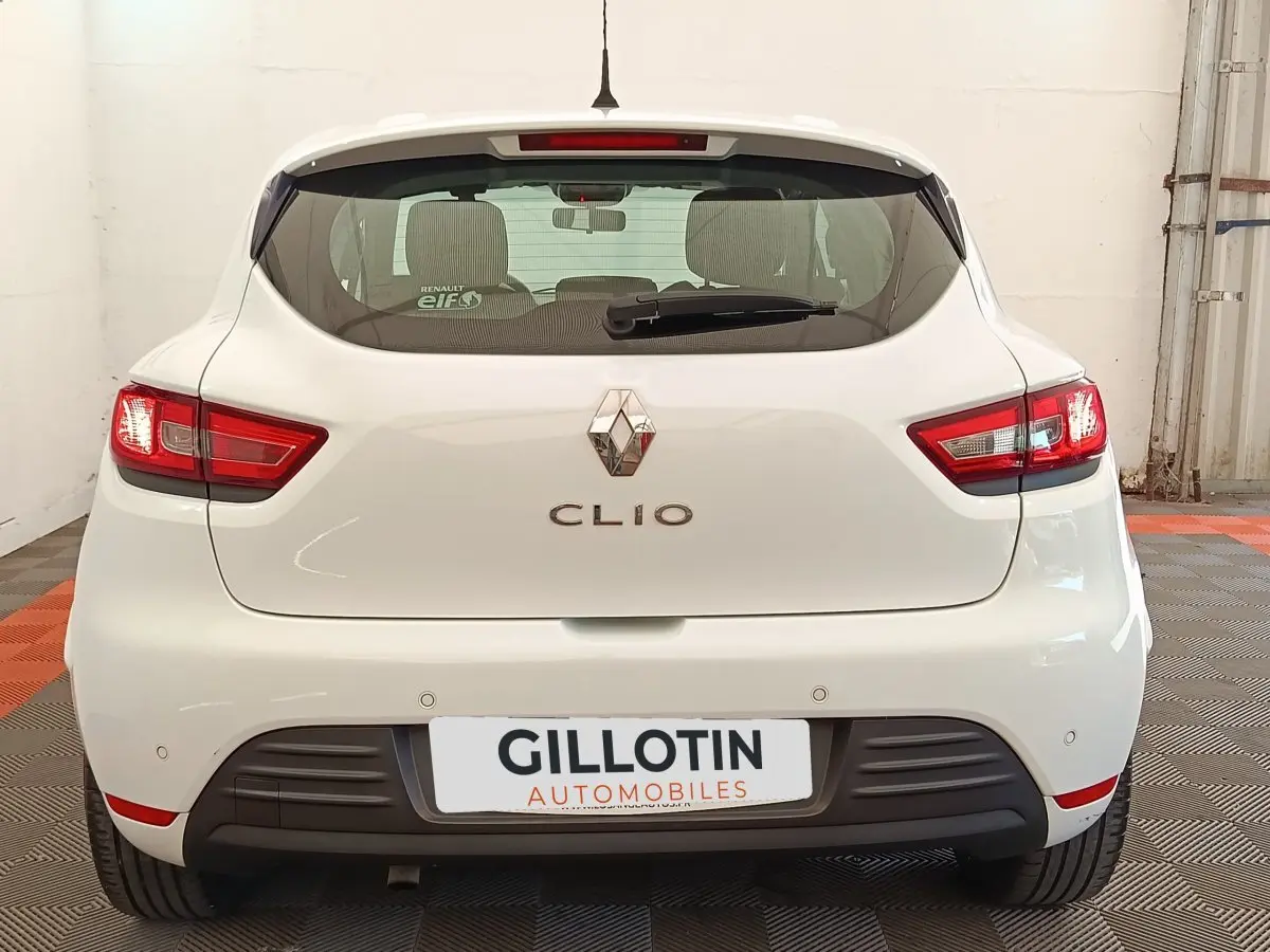Vue arrière d'une Renault Clio blanche de 2018 avec feux arrière allumés et logo Renault visible.