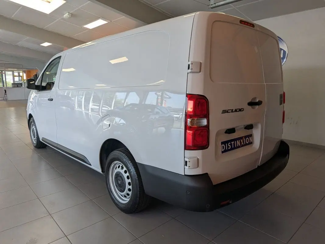 Vue 3/4 arrière droite du fourgon FIAT Scudo blanc avec jantes tôles grises et portes arrière fermées en intérieur showroom.