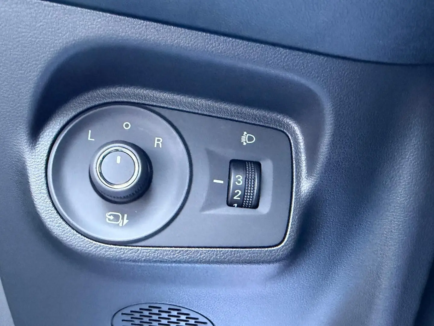 Gros plan sur les commandes de réglage des rétroviseurs et des phares d’un MG3 Pebble Black métallisé, intérieur noir.