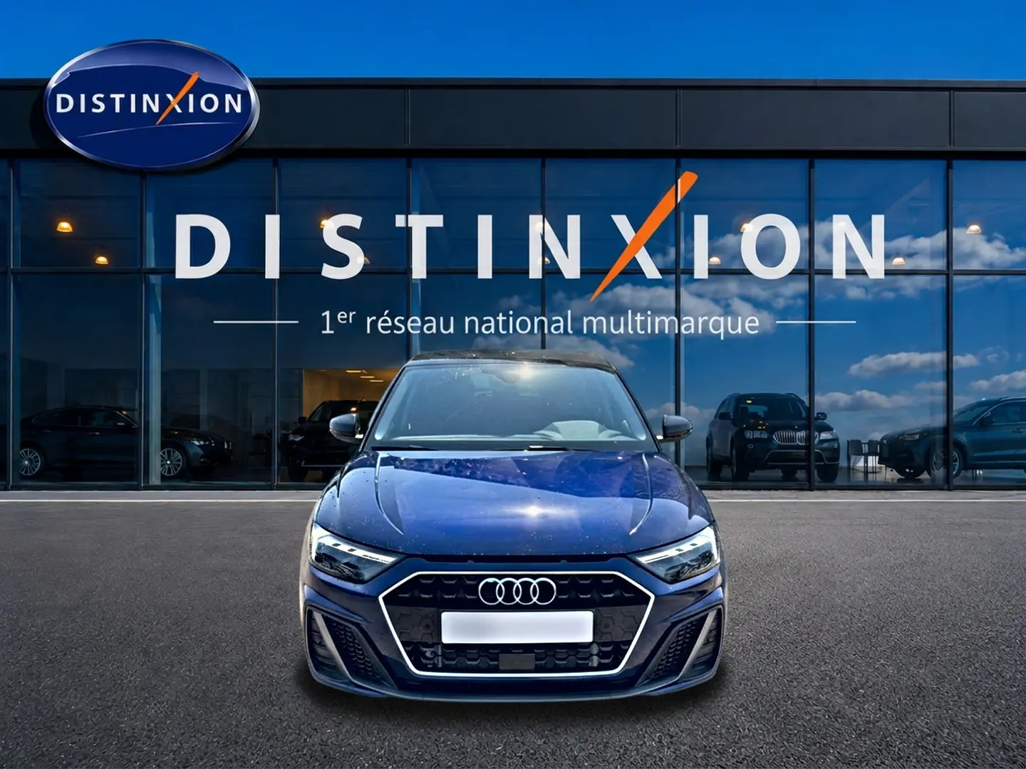 Audi A1 Sportback bleu foncé vue de face, avec calandre hexagonale et phares LED, devant un showroom Distinxion.