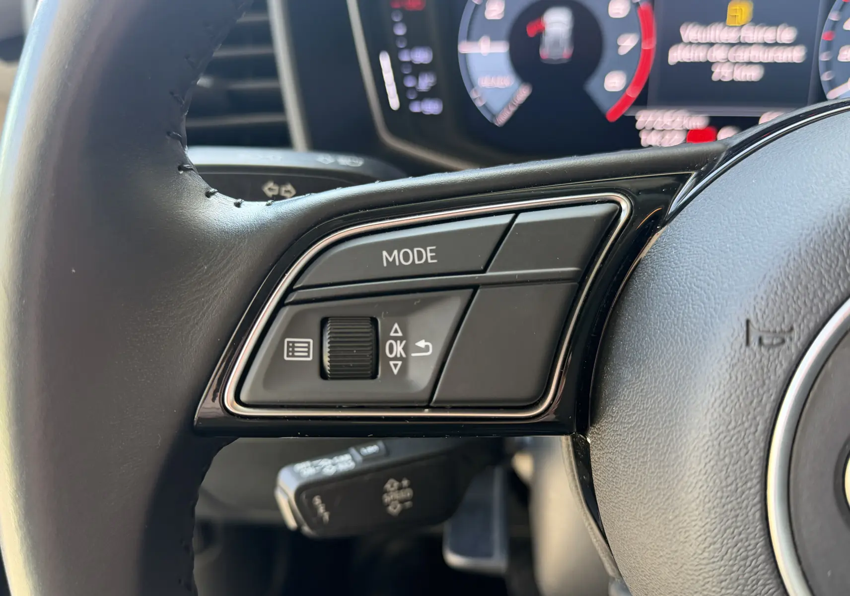 Gros plan sur les commandes gauche du volant noir de l’Audi A1 Sportback 2020, avec affichage numérique en arrière-plan.