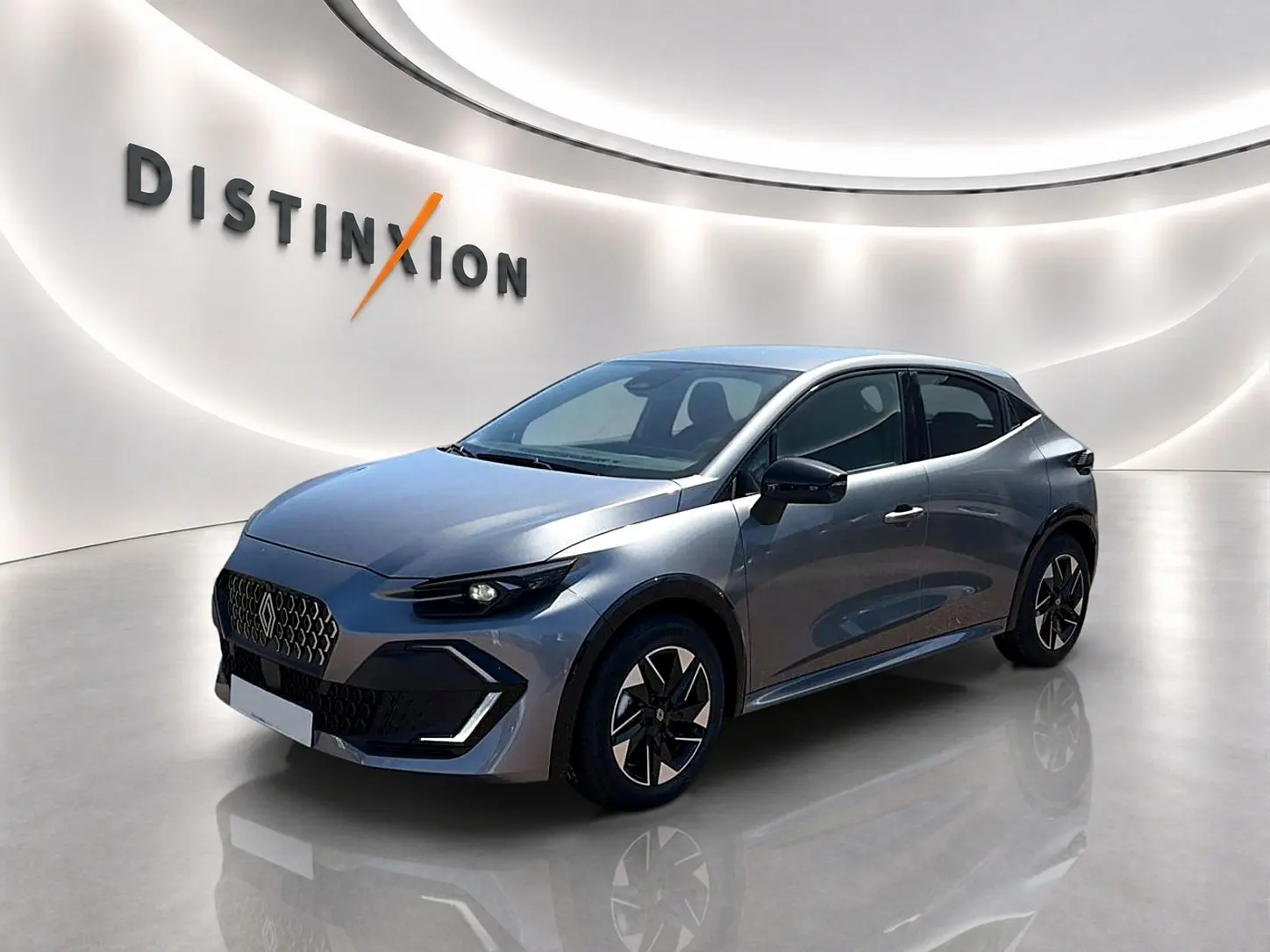Vue 3/4 avant d'une Renault Clio VI gris schiste avec jantes alu et calandre distinctive dans un showroom lumineux.