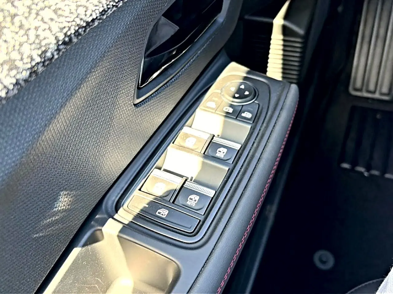 Gros plan sur la commande des vitres électriques côté conducteur avec surpiqûres rouges, intérieur noir de la Renault Clio VI.