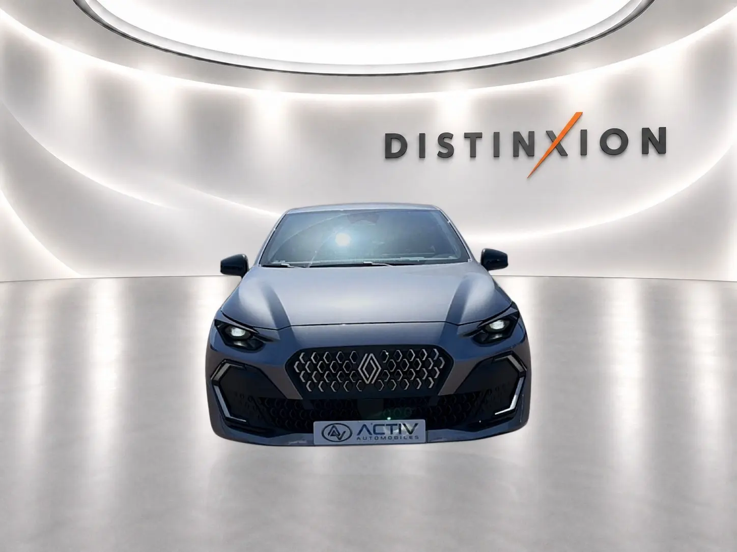 Renault Clio VI gris schiste vue de face dans un showroom avec éclairage moderne et logo Distinxion en arrière-plan.