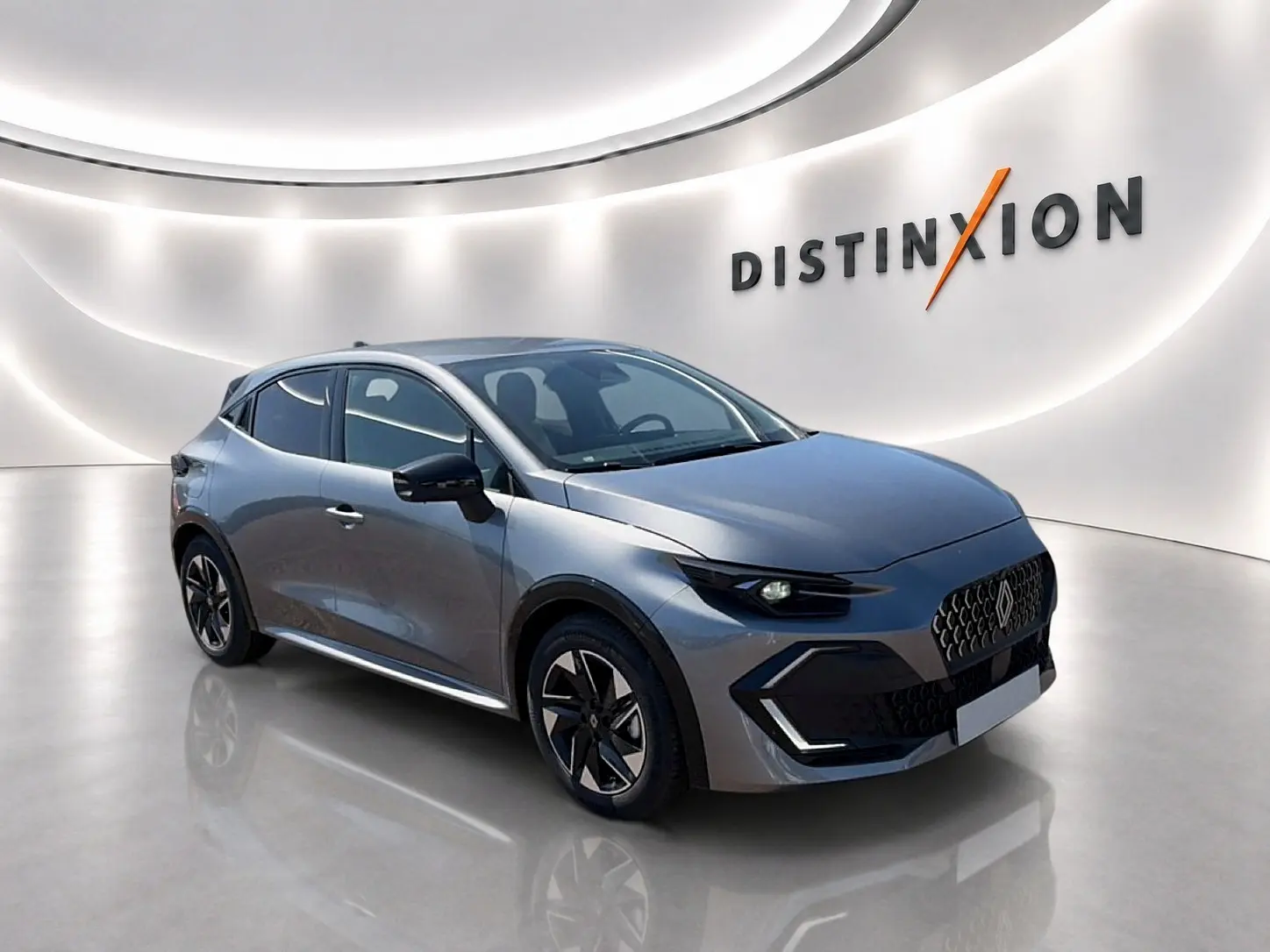 Renault Clio VI gris schiste vue 3/4 avant droit, avec jantes alu et calandre distinctive en showroom lumineux.