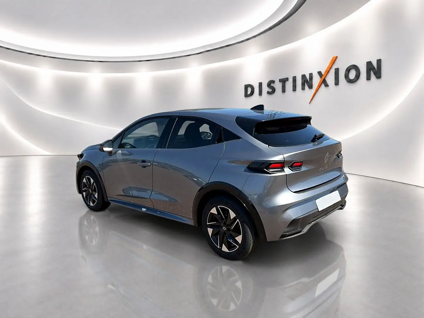 Renault Clio VI gris schiste vue 3/4 arrière droit dans un showroom lumineux avec jantes alu noires.