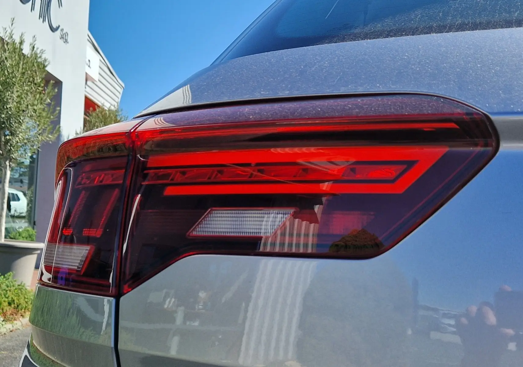 Gros plan sur le feu arrière droit rouge du Volkswagen T-Roc gris pyrite 2023 sous un ciel bleu clair.