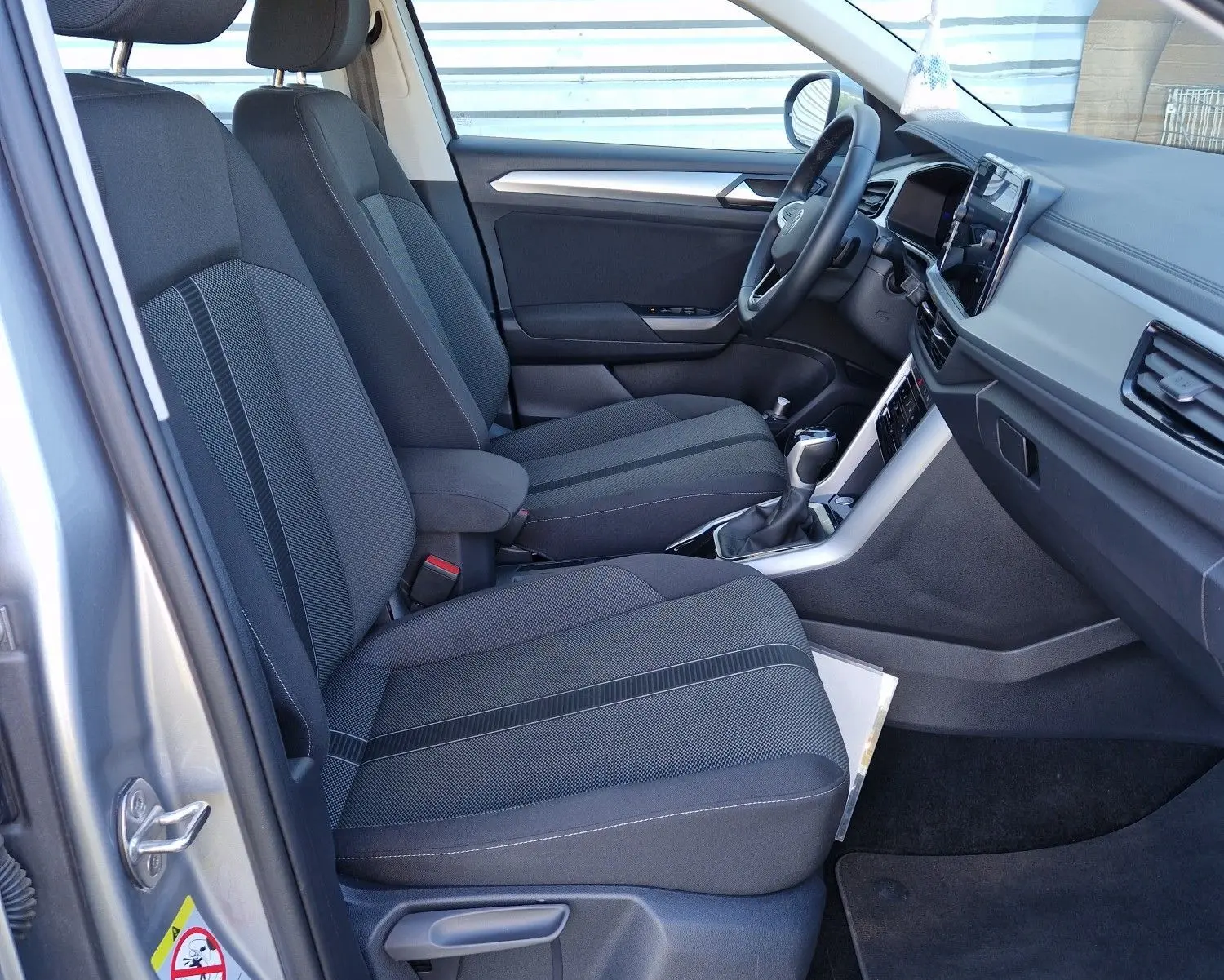 Vue intérieure côté conducteur du Volkswagen T-Roc gris pyrite 2023, mettant en valeur les sièges tissu et le tableau de bord moderne.