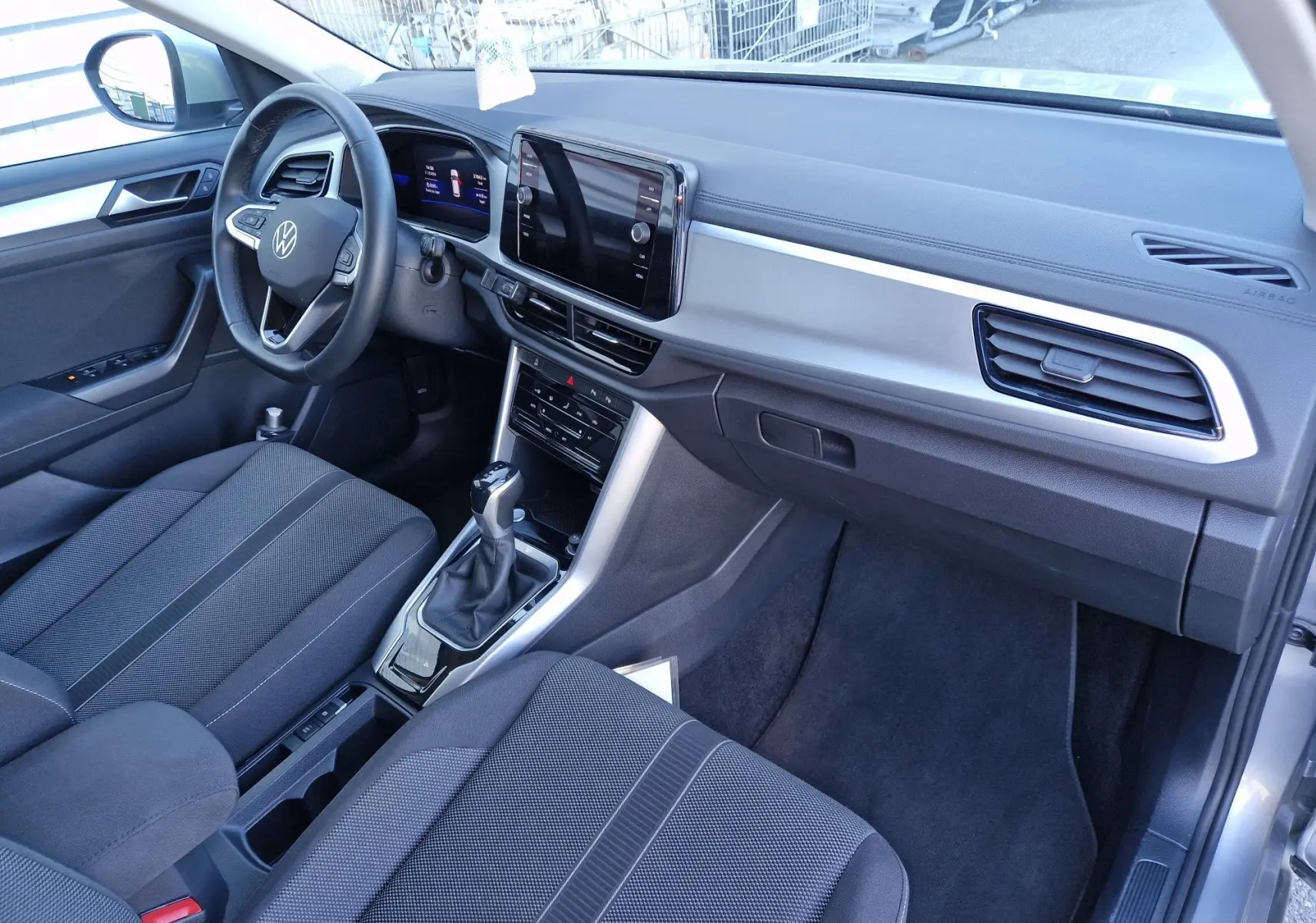 Intérieur du Volkswagen T-Roc 2023 côté conducteur, tableau de bord moderne avec écran tactile et sellerie tissu gris.