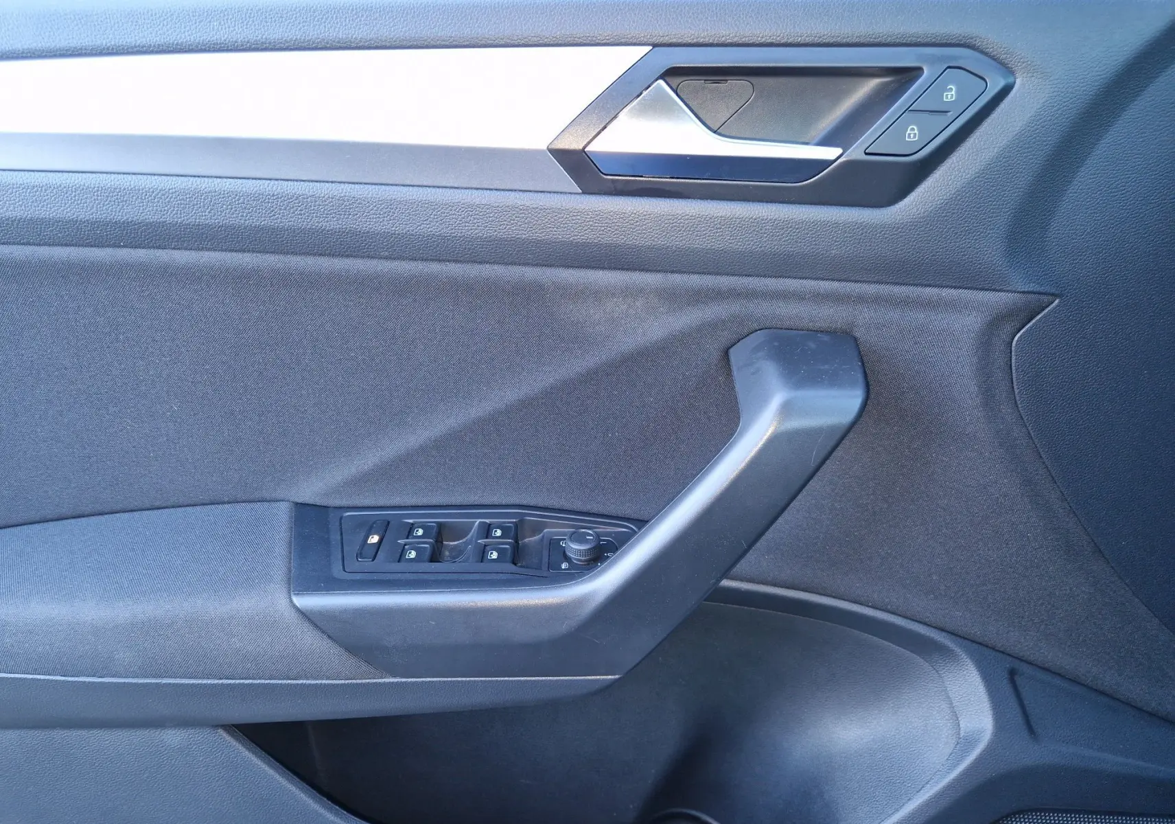 Gros plan sur la porte côté gauche du Volkswagen T-Roc gris Pyrite, montrant les commandes des vitres et la poignée intérieure.
