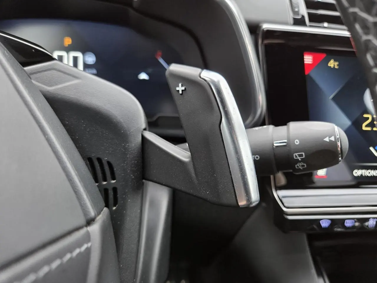 Gros plan sur la palette de changement de vitesse + au volant du DS7 Crossback noir, avec tableau de bord digital en arrière-plan.