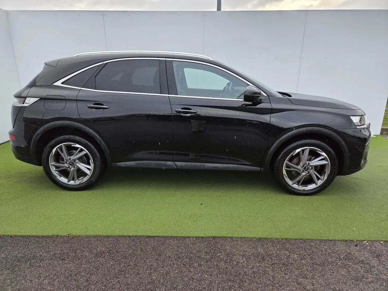 Profil côté gauche du DS7 Crossback noir Perla Metal avec jantes alliage 19 pouces sur fond vert.