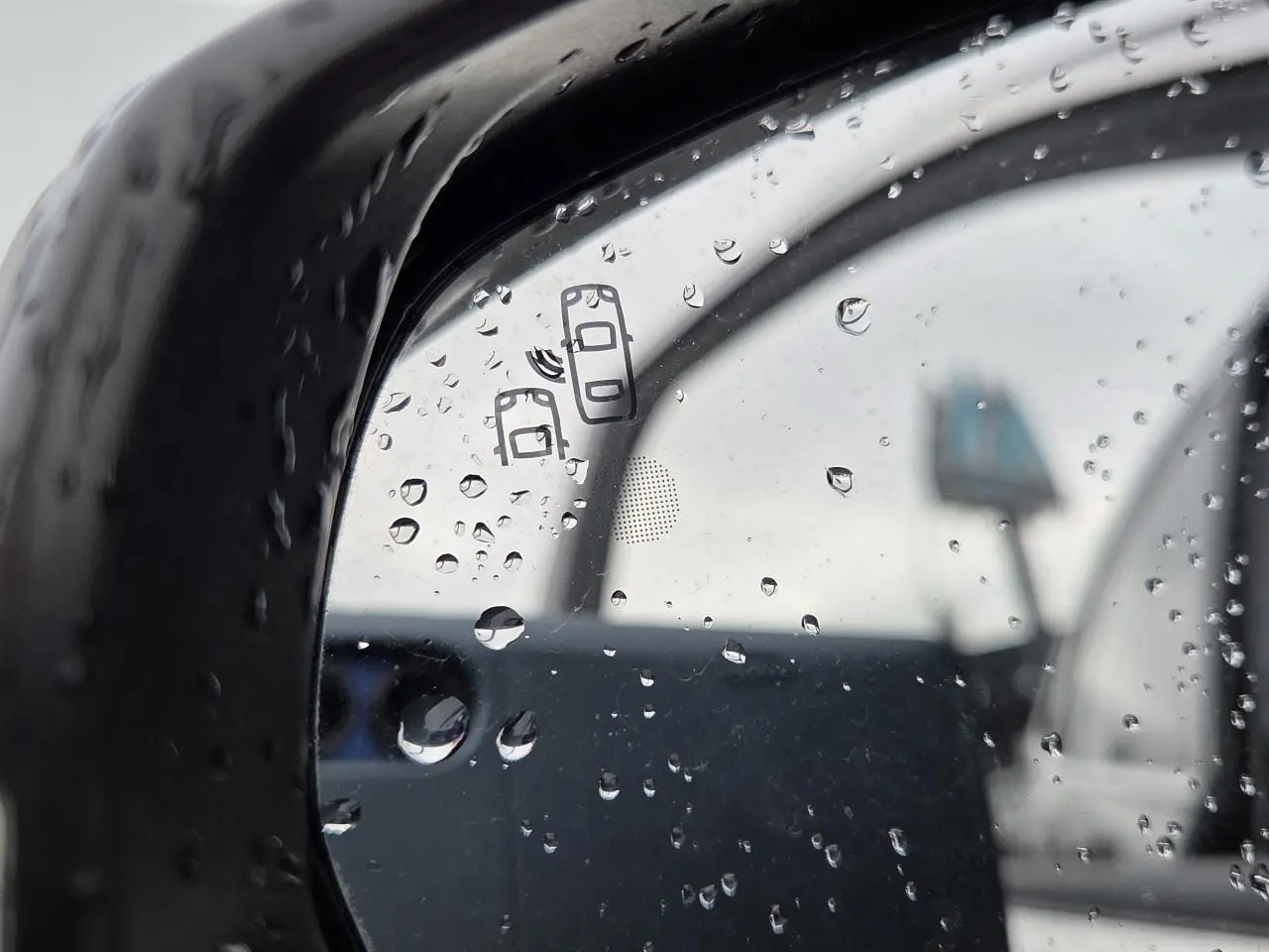 Gros plan sur le rétroviseur côté droit noir perla metal du DS7 Crossback 2022 avec gouttes de pluie et symbole d'alerte d'angle mort.