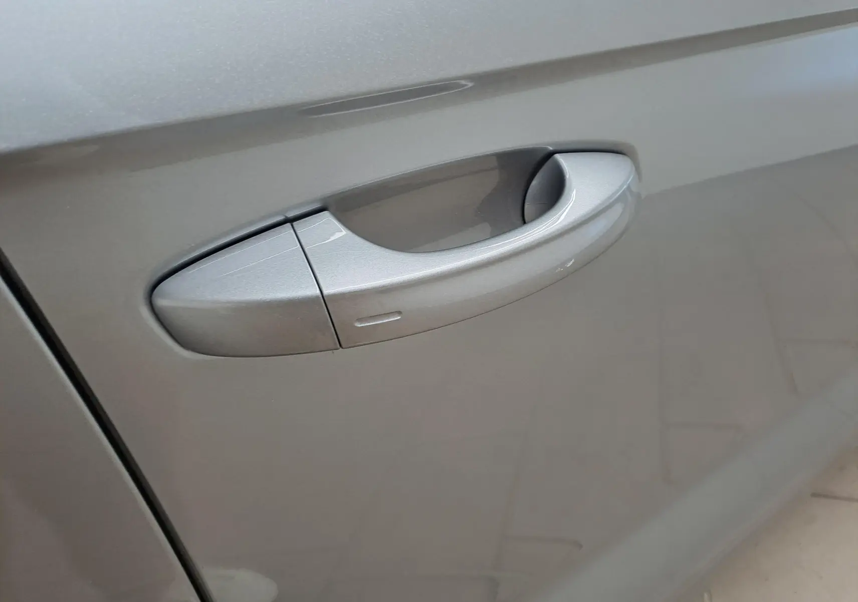 Poignée de porte côté gauche du Volkswagen T-Roc gris pyrite, mettant en valeur la finition lisse et métallisée.